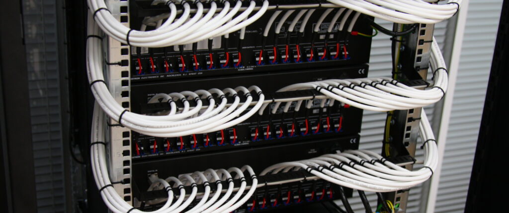 Close-up view of a structured cabling setup featuring neatly organized patch cables and patch panels in a telecommunications room, highlighting efficient network infrastructure.